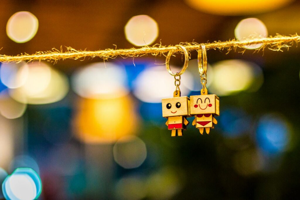 Photo by Chu Chup Hinh Charming wooden cartoon keychain dolls hanging with vibrant bokeh lights in the background, creating a playful and colorful ambiance.
